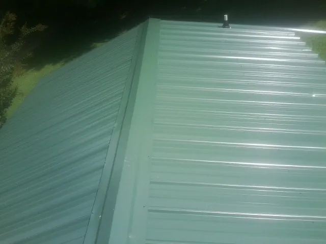 New green metal panels meeting at the ridge of a roof — Flat Roof Repair work by our crew in Pine Island
