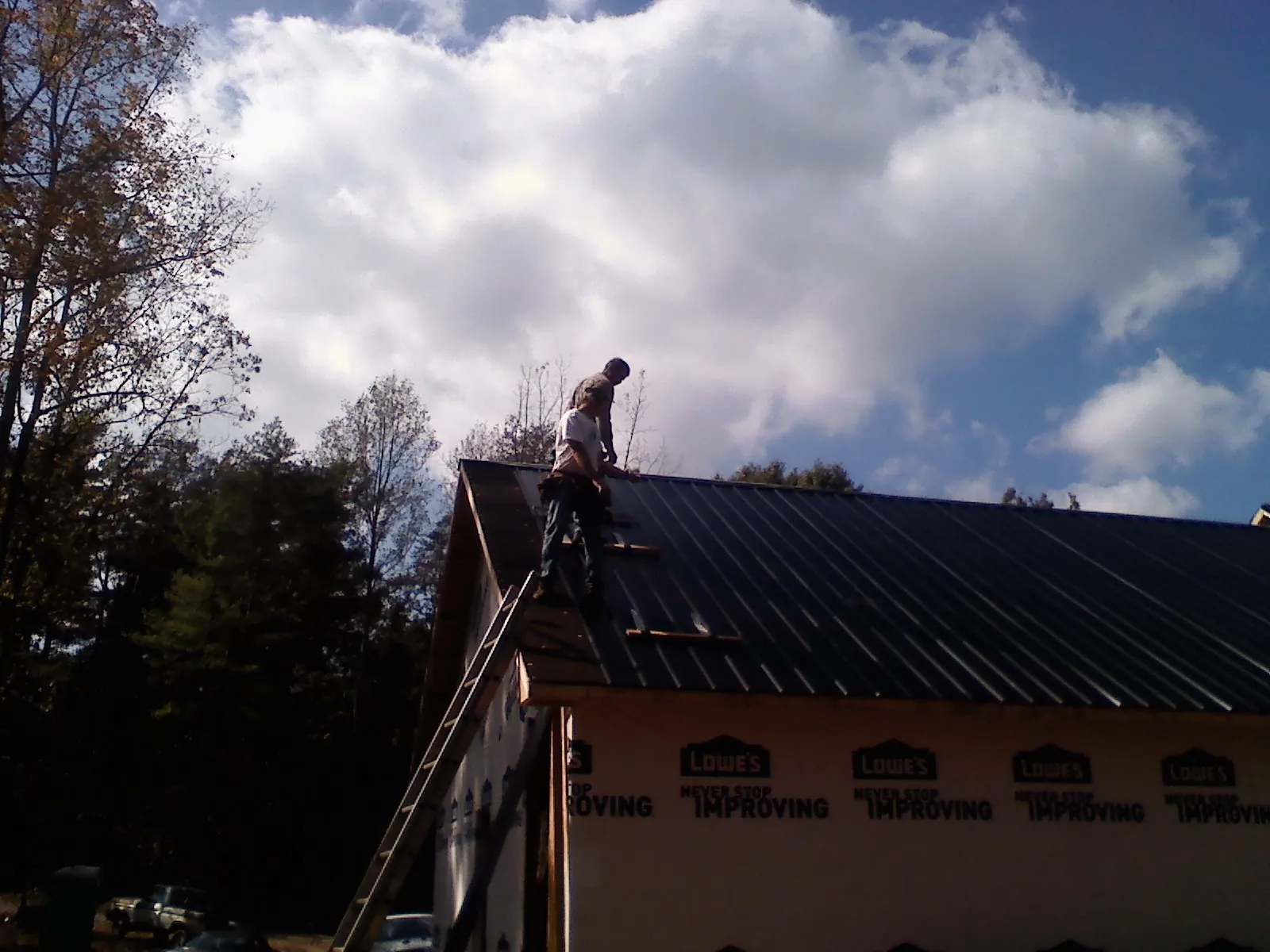 Roofer fastening dark metal panels high against a cloudy sky, from a Roof Inspection job in Pine Island